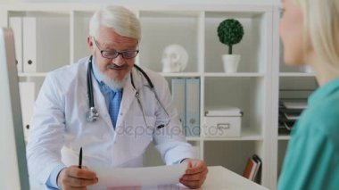 Beyaz orta kağıdın okuma şey genç kadın hastaya gülümseyen erkek doktor ofisinde, oturan gözlüklü yaşlı. Kapalı.