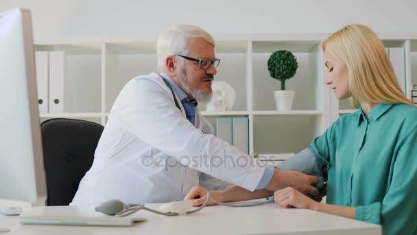 Kaukaski poważny mężczyzna lekarz siedzi w jego offise, pomiaru ciśnienia krwi kaukaski młody pacjent piękne female. Wewnątrz. — Wideo stockowe