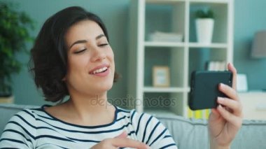 Genç kadın evde kanepede otururken ona hareket eden smartphone üzerinde onun arkadaşı ile görüntülü görüşme sahip. Yakın çekim