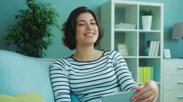 Mujer atractiva sentada en el sofá sonriendo y mirando directamente a la cámara. Retrato plano — Vídeos de Stock