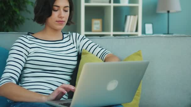 Junge brünette Frau arbeitet mit Laptop und telefoniert zu Hause mit ihrem Handy — Stockvideo