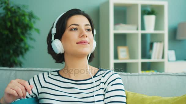 Крупним планом красива молода жінка слухає музику у великих білих навушниках. Жінка посміхається і рухається до ритму — стокове відео