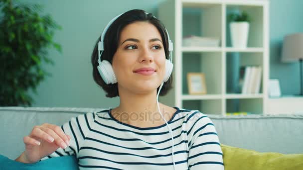 Закрыть привлекательную молодую женщину, слушающую музыку в больших белых наушниках. Женщина улыбается и движется к ритму — стоковое видео