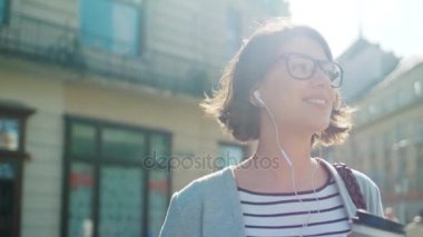 Şehir sokakta yürüme ve müzik onun akıllı telefon üzerinde çekici genç kadın. Güneşli bir gün. Açık havada