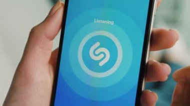New York - 10 Şubat 2017: Kadın el nasıl evde kanepede yatan yaparken müzik arama için akıllı telefon Shazam uygulamasını kullanarak. Yakın çekim.