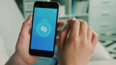 New York - 10 Şubat 2017: Nasıl evde oturma odasında kanepede yatan yaparken müzik arama için akıllı telefon Shazam uygulamasını kullanarak kadın eller.