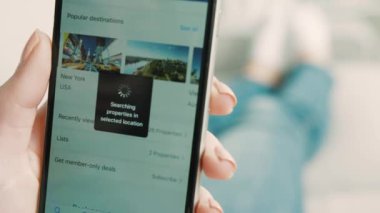 New York - 10 Şubat 2017: kadın el gezi uygulama akıllı telefon gelecekteki seyahat için seaching oteldeki Koç oturma odasında yatan süre kullanarak. Yakın çekim.