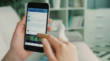 New York - 10 Şubat 2017: kadın kanepede yatan süre burada acount akıllı telefon üstünde Facebook beslemeleri tarama. Atış kapatın.