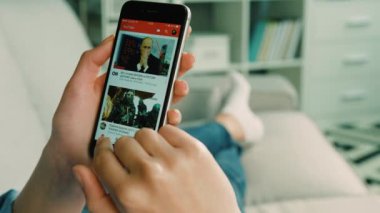 New York - 10 Şubat 2017: koltukta evde dinlenirken genç hareket eden app, video izlemek için cep telefonu kullanan genç kadın. Yakın çekim.