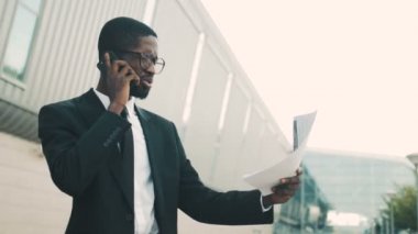 Çekici Afrikalı-Amerikalı işadamı belgeleri, kağıtları tutan cep telefonuyla konuşuyor. İş adamı bağıran adam kızgın, hayal kırıklığına ve tatminsiz, arıyorum. Sorunları çözme. Yakın çekim