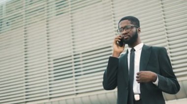 Cep telefonuyla konuşurken ve cebinde duran ofisinin koyarak çekici genç Afro-Amerikalı işadamı Merkez bina. Yakın çekim