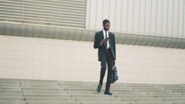 Merdivenlerden aşağı yürüme çekici siyah Afrika kökenli Amerikalı iş adamı adımları, akıllı telefon kullanarak. Sms, okuma adam İnternet'te sörf