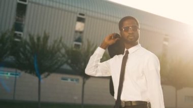Ceket omzunun üstünde tutarak ve gülümseyen office merkezine yakın yürüme çekici siyah Afrika kökenli Amerikalı iş adamı. Adam işten sonra eve gidiyorum. Güneş ışınları. Yakın çekim