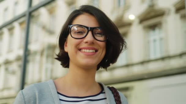 美丽的女人戴着眼镜，微笑着把镜头对准了城市街道的脸肖像。关闭 — 图库视频影像