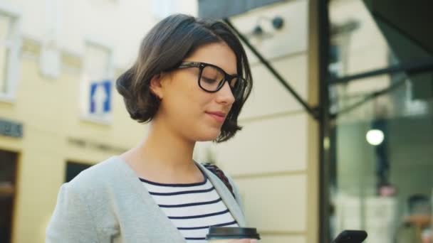 Mujer caminando por la calle y usando un teléfono inteligente. Mujer bebiendo café. De cerca. — Vídeos de Stock