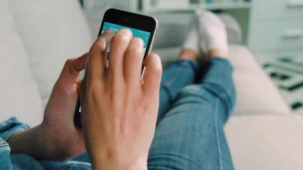 New York - March 10, 2017: Woman hands using Amazon on the smart phone for searching the clothe in online shop while lying on the coach in the living room at home. Close up. — Stock Video