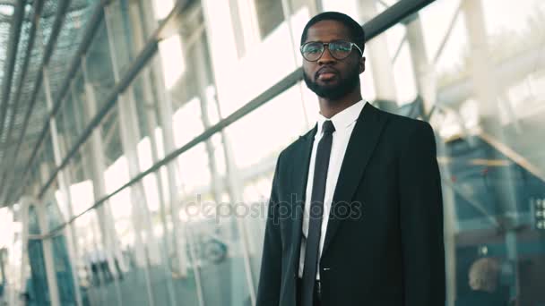 Retrato de um jovem empresário negro afro-americano perto de grandes janelas de escritórios e olhando diretamente para a câmera. Centro de negócios . — Vídeo de Stock