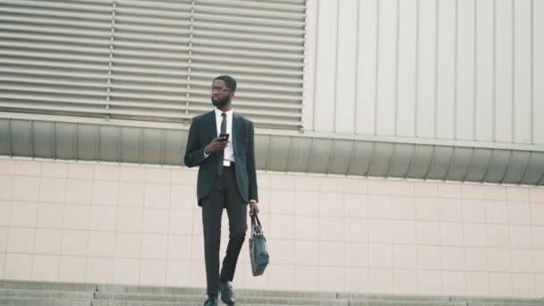 Atractivo hombre de negocios negro bajando las escaleras, escalones, usando un teléfono inteligente. Hombre leyendo sms, navegar por Internet — Vídeo de stock