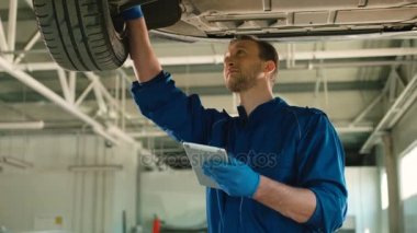 Beyaz genç konsantre otomatik mekanik adam cheking araba tekerlek ve tablet vasıl autoservice yazarak durumu. Kapalı.