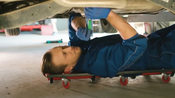 Zijaanzicht van portret van Kaukasische jonge mooie auto monteur man bevestiging van de schroeven in de onderkant van de auto bij autoservice. Indoor. — Stockvideo