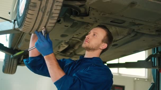 Porträt eines kaukasischen jungen Automechanikers in blauer Uniform, der am Autoservice steht und einen Steckschlüssel in der Hand hält. Innenräume. — Stockvideo