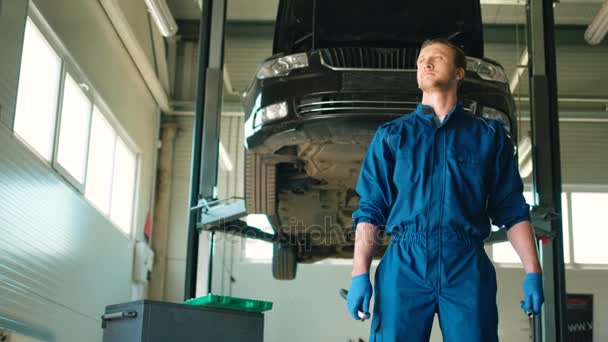 Kaukasische jonge auto monteur man in blauwe uniform permanent bij autoservice en houden van moer socket moersleutel. Indoor. — Stockvideo