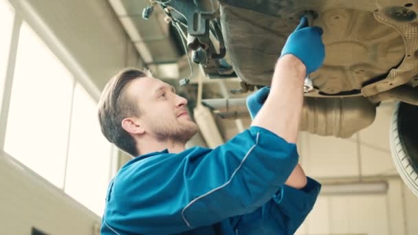 Widok z boku kaukaski piękne auto mechanik człowieka za pomocą nakrętki nasadowe do mocowania śruby na dole samochodów o autoservice. Wewnątrz. Z bliska. — Wideo stockowe