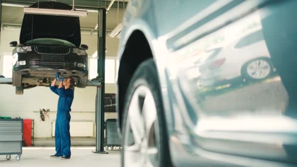 Kaukasischer gutaussehender Automechaniker, der beim Autoservice die Schrauben per Mutternschlüssel in den Wagenboden schraubt. Innenraum. Seitenansicht. — Stockvideo