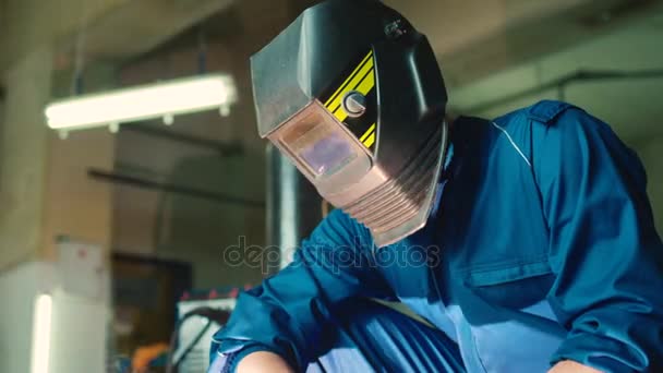 Auto monteur man op autoservice achtergrond in blauwe uniform en lassen helm met behulp van lassen apparaat. Indoor. — Stockvideo