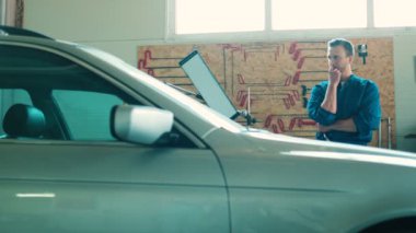 Beyaz genç otomatik mekanik içinde mavi üniforma proping yüz autoservice, el durarak gebe. Kapalı.