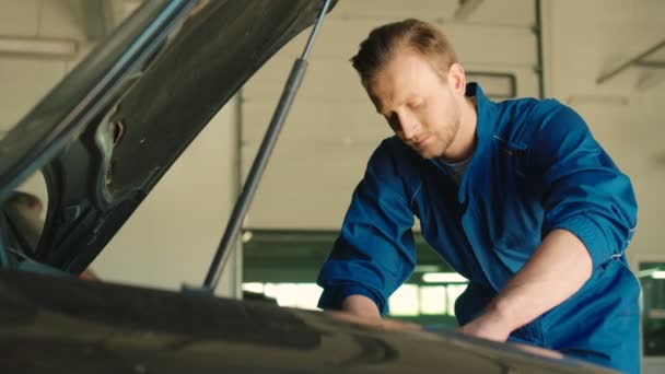 Koncentrované mladý bělošský auto mechanik člověka nuting v háji pod kapotou vozu, pomocí nástrčného matice. Vnitřní. — Stock video