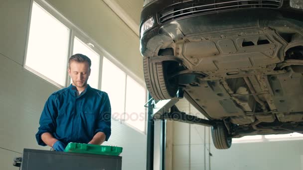 Młody skoncentrowane kaukaski auto mechanik mężczyzna stojący w autoservice i komponowania z nakrętki klucz nasadowy. Wewnątrz. — Wideo stockowe