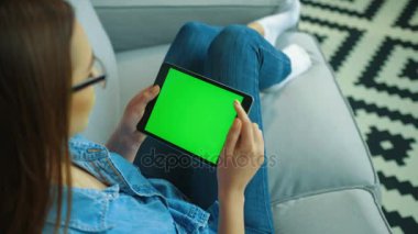 Oturma odasında kanepede otururken ile yeşil ekran siyah tablet bilgisayar kullanan genç kadın. Kaydırma, yakınlaştırma sayfaları eller kadın. Chroma anahtar. Üstten Görünüm