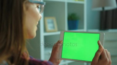 Oturma odasında kanepede otururken ile yeşil ekran beyaz tablet bilgisayar kullanan genç kadın. Kaydırma, sayfaları swiping eller kadın. Chroma anahtar. Arka yan görünüm. Yakın çekim