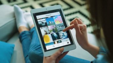 New York - 15 Mayıs 2017: kadın fotoğrafları, oturma odasında kanepede otururken Instagram app profillerinde kaydırma. Tablet aygıtı kullanan kadın. Yakın çekim. Omuz üzerinden vurdu