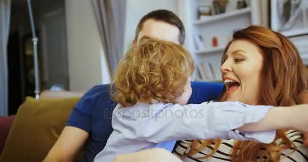 Famiglia felice seduta insieme sul divano del soggiorno. Padre, madre e figlio seduti sul divano. Figlio che abbraccia i suoi genitori. momenti felici — Video Stock