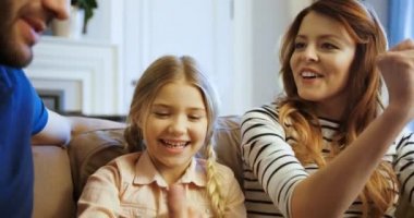 Mutlu aile, oturma odasında kanepede birlikte eğleniyor. Baba, anne ve kızı kanepede oturan, dinlenme, oyun oynamak ve gülüyor.