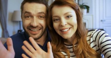 Mutlu genç aile kayıt dizüstü bilgisayarda kameraya el sallayarak, oturma odasında kanepede oturan video kapatmak. Üzerinde arkadaşlarınızla konuşurken erkek ve kadın online video sohbet, skyping,