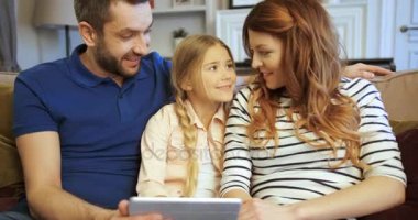 Anne, baba ve kızı kullanarak tablet, oyun oynamak ve eğlenmek. Evde birlikte vakit aile. Mutlu bir aile