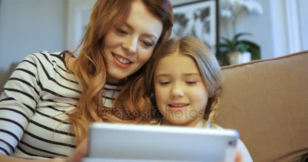 Attractive mother with daughter using tablet computer. Mother and daughter sitting on the sofa at the living room and playing with tablet device. Close up — Stock Video