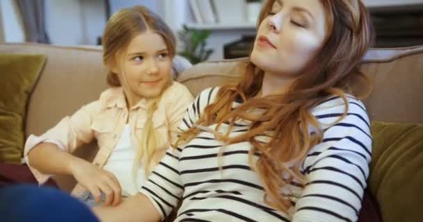 Heureuse femme attirante avec sa fille passer du temps ensemble à la maison sur le canapé. Mère et fille souriant, embrassant et riant . — Video