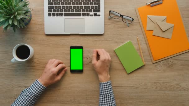 Muž chytrý telefon pomocí zeleným plátnem na dřevěný stůl pozadí. Male ruce posouvání stránky, zvětšení, klepněte na dotykovou obrazovku. pohled shora. Materska v pozadí stolu. Chroma klíč. — Stock video