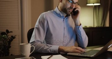 Çekici genç adam ofiste cep telefonuyla konuşuyor. Ofiste dizüstü bilgisayar üzerinde çalışan bir genç adam. Geç saate kadar