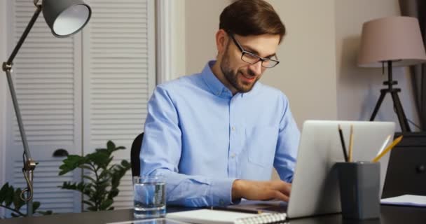 Atractivo hombre de negocios escribiendo en su portátil. Joven sonriendo y posando en cámara . — Vídeos de Stock