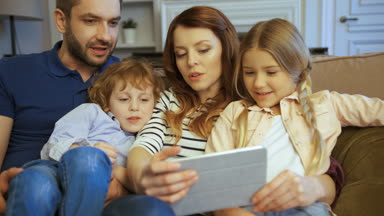 Anne, baba, oğlu ve kızı kullanarak tablet, film izlemek, oyun oynamak, dokunarak ve dokunmatik ekran kaydırma. Evde birlikte vakit aile. Mutlu bir aile