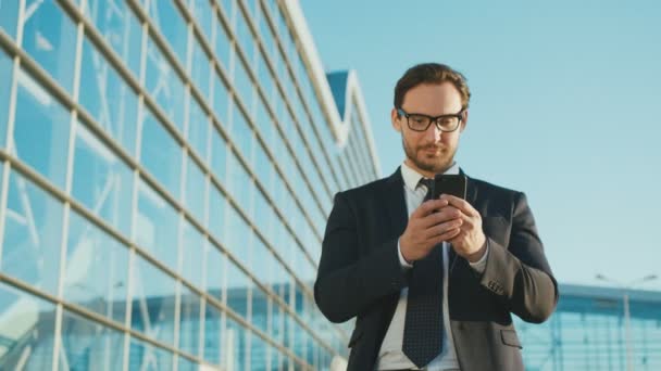 Gyönyörű kaukázusi busineesman használ smartphone állva, az irodán kívül középre épület. Ember, olvasás, gépelés-on sejt telefon. Közelről — Stock videók