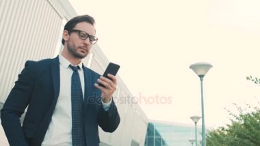 Açık havada office ayakta iken Smartphone kullanarak çekici genç işadamı Merkezi bina. Adam okuma, manifatura üstünde hareket eden telefon. Yakın çekim