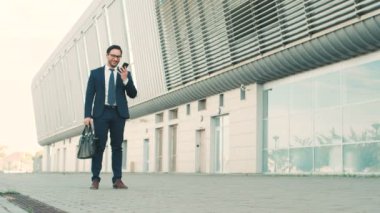 Şık beyaz işadamı cep telefonuyla konuşurken, bakarak ve ofis Merkezi Binası yakınındaki bir toplantı için çalıştırıyor. Adam işe geç toplantı. Ağır çekim.