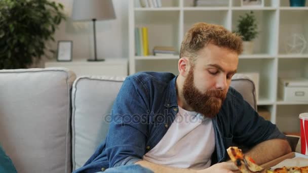 Homem atraente em casa camisa comer pizza enquanto assiste tv em casa na sala de estar . — Vídeo de Stock