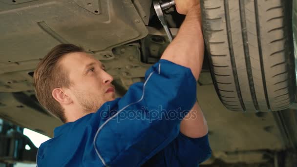 Portrait of young auto mechanic man using nut socket wrench for nuting of the screwed into wheel mechanism of car. Indoor. — Stock Video